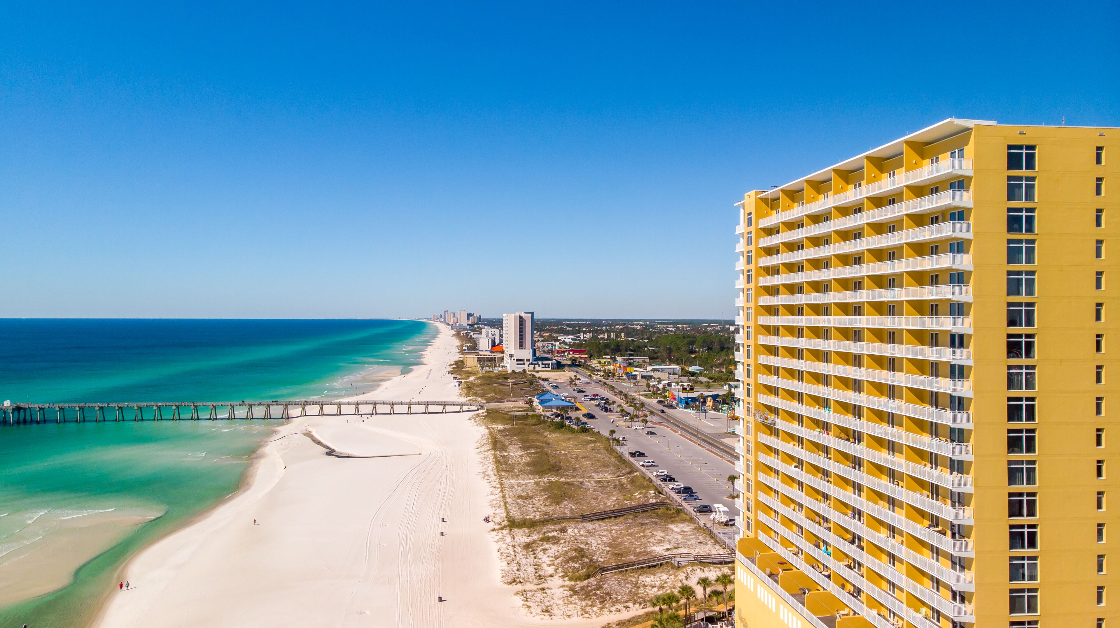 A coastal hotel with a beach view, a pier, and a road leading to the beach.