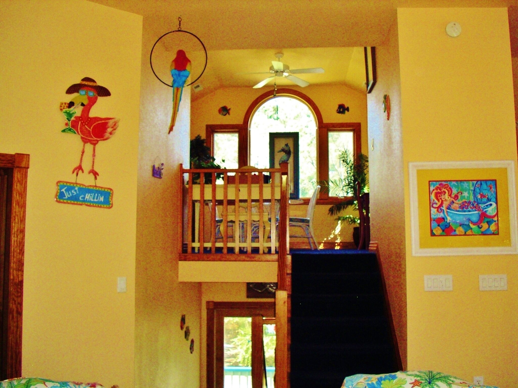 Habitación con escalera de madera, ventilador de techo y ventana con vista a follaje.