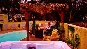 A hot tub with lounge chairs and a thatched roof structure in a backyard setting. - TIKI POOL & SPA, GOLF CART, KAYAK, WATERFALL, FIREPIT EXCELLENT LIGHTHOUSE VIEWS (Corolla)