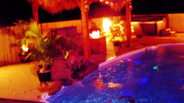 A nighttime view of a pool area with a thatched structure and potted plants. - TIKI POOL & SPA, GOLF CART, KAYAK, WATERFALL, FIREPIT EXCELLENT LIGHTHOUSE VIEWS (Corolla)