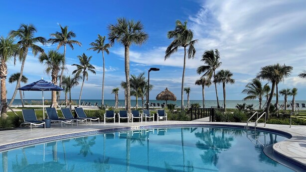 Una piscina con acqua cristallina, circondata da palme e lettini, con vista sull'oceano.