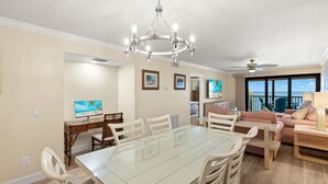 Un'ampia sala da pranzo con tavolo e sedie in vetro, un lampadario e vista sull'oceano attraverso ampie finestre.