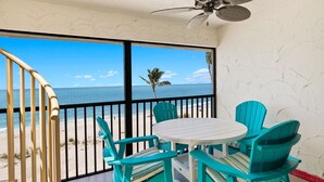 Un balcone con vista sulla spiaggia e sull'oceano, sedie turchesi, un tavolo bianco e una ventola a soffitto.
