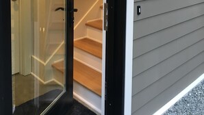 A modern house entrance with a glass door, a wooden staircase, and a wall-mounted light fixture.