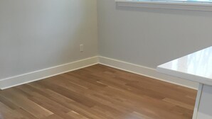 A room with a wooden floor, white walls, and a window with blinds.