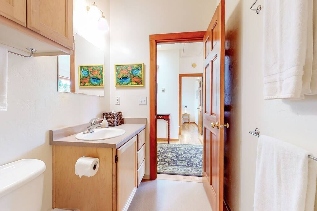 A narrow hallway leading to a bathroom with a sink, toilet, and a door leading to another room.