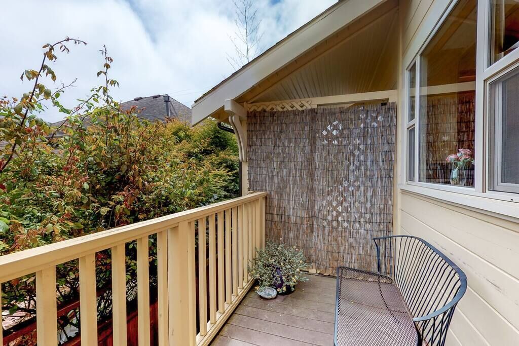 A covered balcony with a wooden railing, a metal chair, and a potted plant.