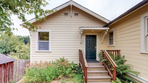 A single-story house with a front porch, a front door, and a small front yard with plants and a wooden fence.