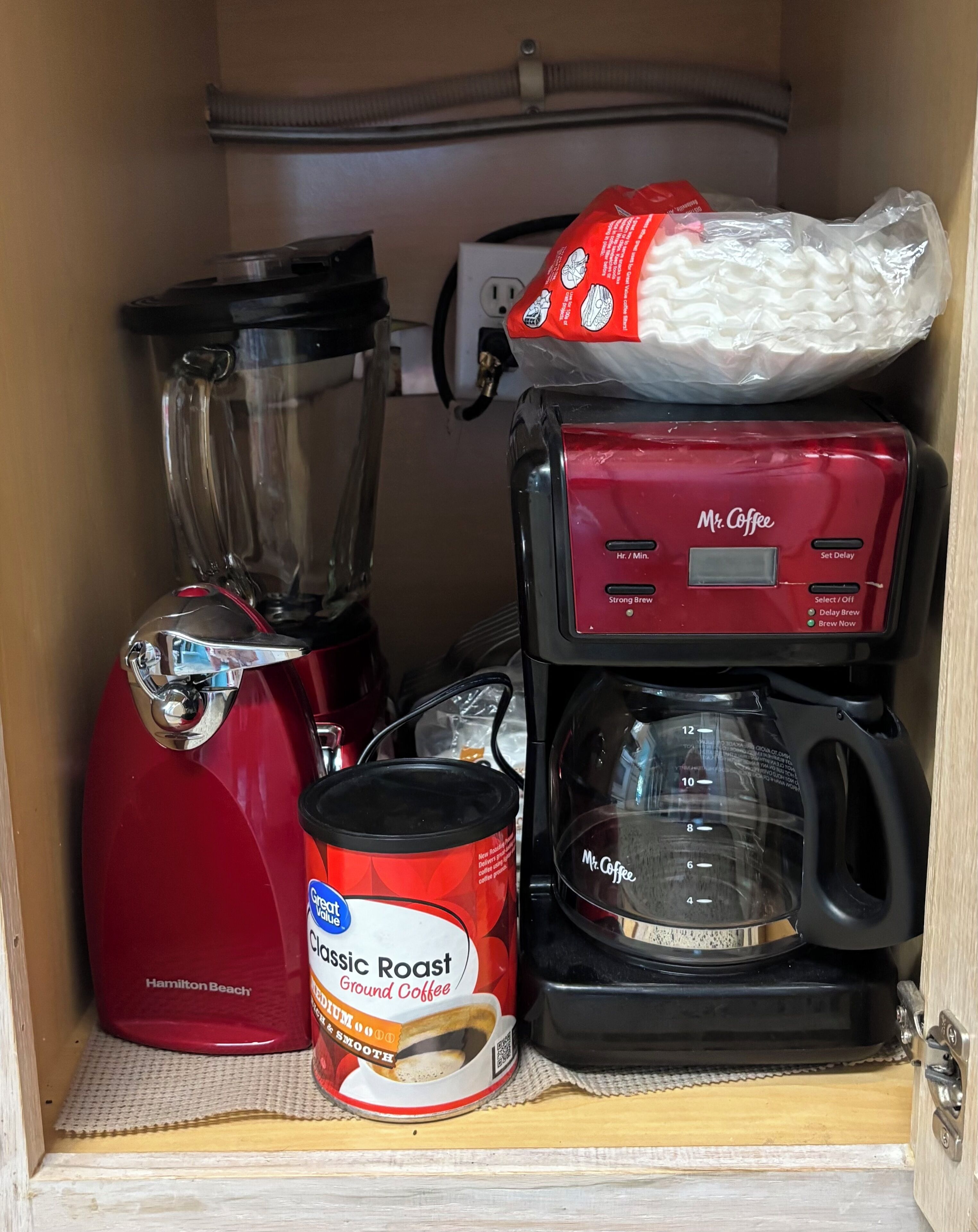 Una zona de cocina con una cafetera roja Mr. Coffee, una licuadora, una jarra de café Mr. Coffee y una lata de café molido Hamilton Beach.