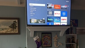 Ett vardagsrum med en platt-TV som är monterad ovanför en öppen spis och som visar gränssnittet för en streamingtjänst.