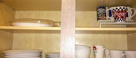 A kitchen shelf with various dishes and mugs.
