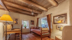 A cozy bedroom with a wooden bed, a desk, a chair, a window with curtains, and a mirror on the wall.
