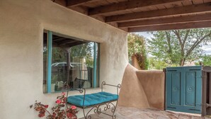 A covered patio with a bench, a potted plant, and a view of the outside.