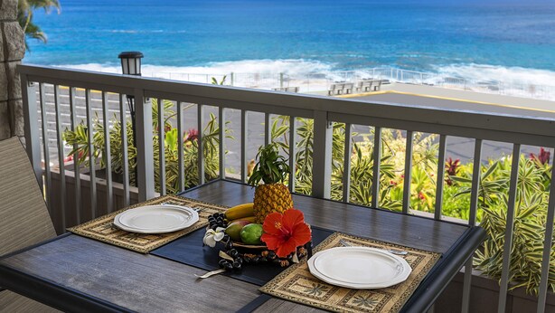 A dining table with a tropical fruit arrangement and a view of the ocean.