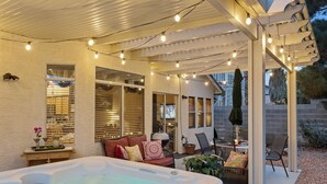 Un patio cubierto con jacuzzi, mobiliario exterior, luces colgantes y una pérgola.