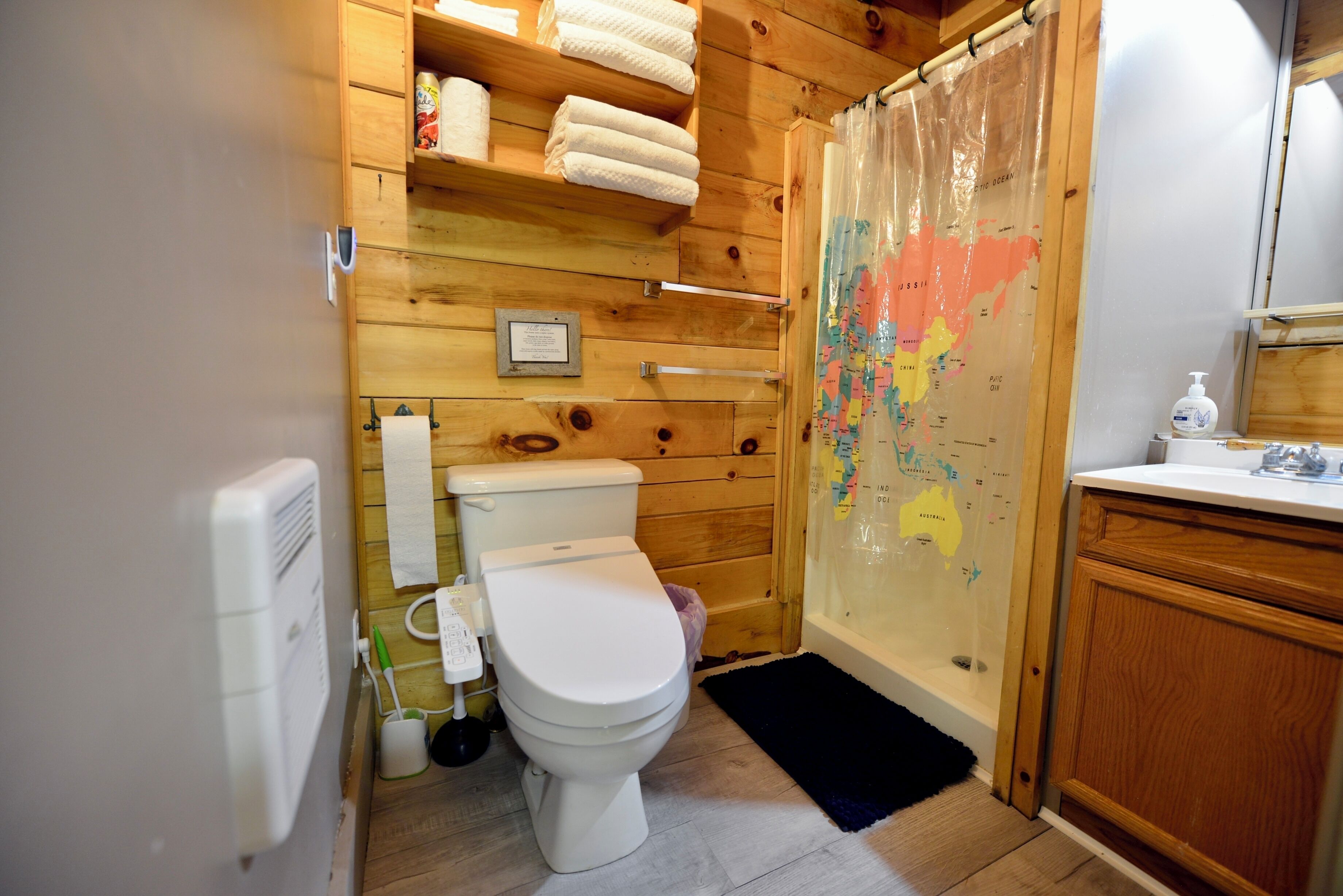 A wooden-paneled bathroom with a toilet, a shower curtain with a map, and a wooden cabinet.