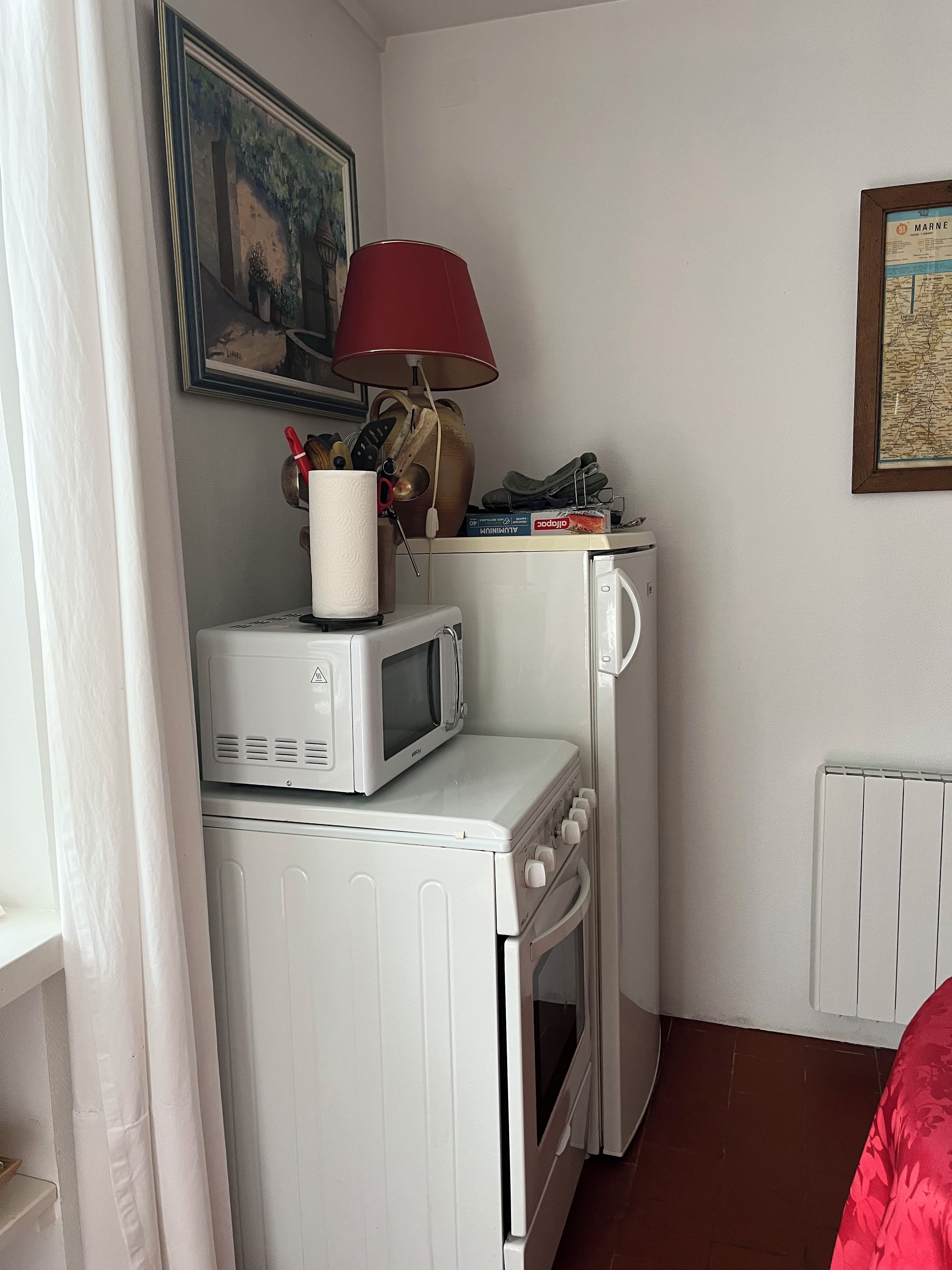 Eine kompakte Küche mit Mikrowelle, Toaster und Backofen. An der Wand befinden sich eine rote Lampe und eine gerahmte Karte.