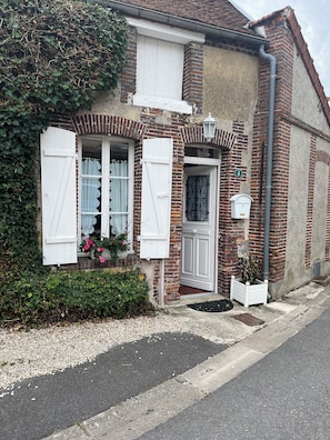 Ein zweistöckiges Haus mit Backsteinfassade, weißen Fensterläden und einem kleinen Garten mit rosa Blumen.