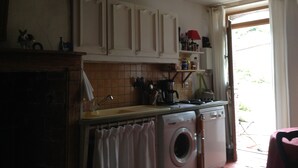 Une cuisine avec des meubles blancs, un lave-linge et une fenêtre avec des rideaux.