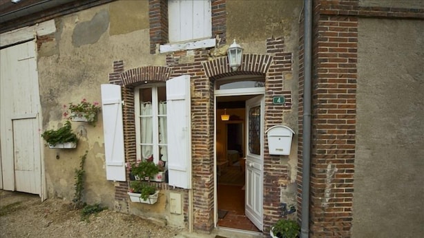Un bâtiment de style rustique, avec une façade en briques, des volets blancs et une petite entrée.