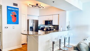 A modern kitchen with a central island, stainless steel appliances, and bar stools. - 🌴 Rare Double Gulf View~Free Beach Chairs~No Resort Fee~2nd floor Front Parking (Panama City Beach)