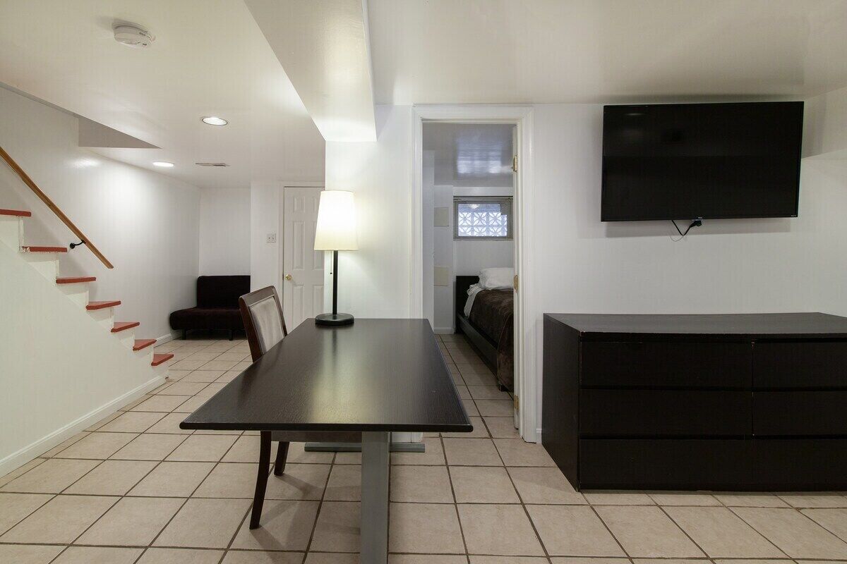 A modern living room with a dining table, a sofa, a TV mounted on the wall, and a staircase with red steps.