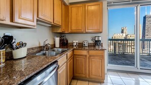 A kitchen with wooden cabinets, granite countertops, stainless steel appliances, and a view of a cityscape through a large sliding glass door. - 55th-Floor 3BR Duplex Penthouse  Lake & City Views (Chicago)