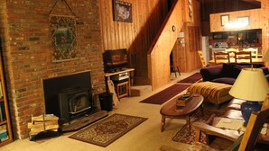 A cozy living room with a fireplace, wooden walls, a sofa, and a dining area. - Spa, Quiet, Peaceful Near Rollins Lake, Local Hiking, Romantic, Reunion, Retreat (Gold Run)