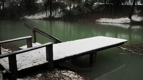 Eine mit Schnee bedeckte Holzstege, der sich in ruhiges Gewässer erstreckt, umgeben von Bäumen.