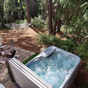 Ein Whirlpool in einer bewaldeten Gegend mit einer Hängematte und Stühlen in der Nähe.