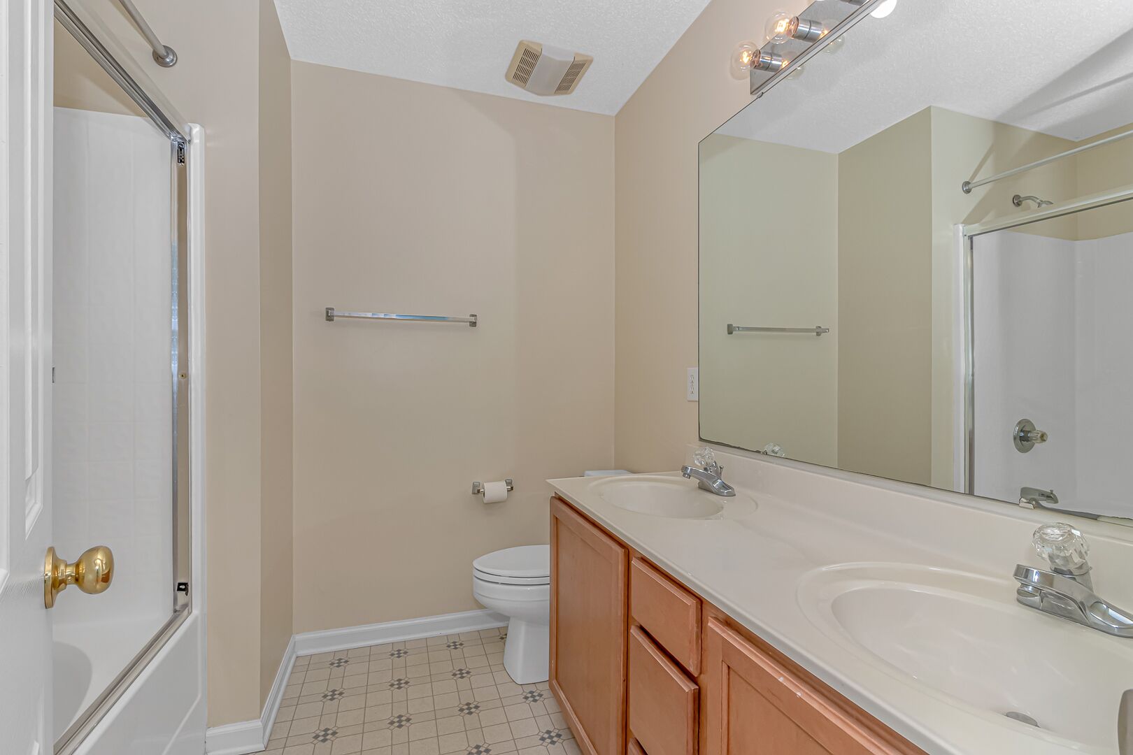 Une salle de bain comprenant des toilettes, un lavabo, un miroir, un porte-serviettes et une porte de douche.