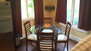 A dining area with a glass table surrounded by wooden chairs, a bowl of fruit, and a refrigerator. - Tuscan Villa with Private Courtyard in Briarbrook (near Joplin Regional Airport) (Carl Junction)