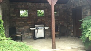 A stone patio with a barbecue grill, two chairs, and a wooden pergola. - Tuscan Villa with Private Courtyard in Briarbrook (near Joplin Regional Airport) (Carl Junction)