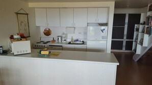 Een kleine keuken met witte kasten, een fornuis, een koelkast en een koffiezetapparaat.