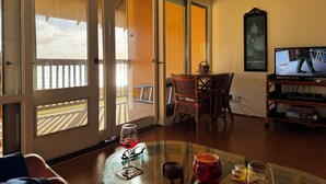 Een woonkamer met een glazen tafel, een televisie en uitzicht op een balkon.