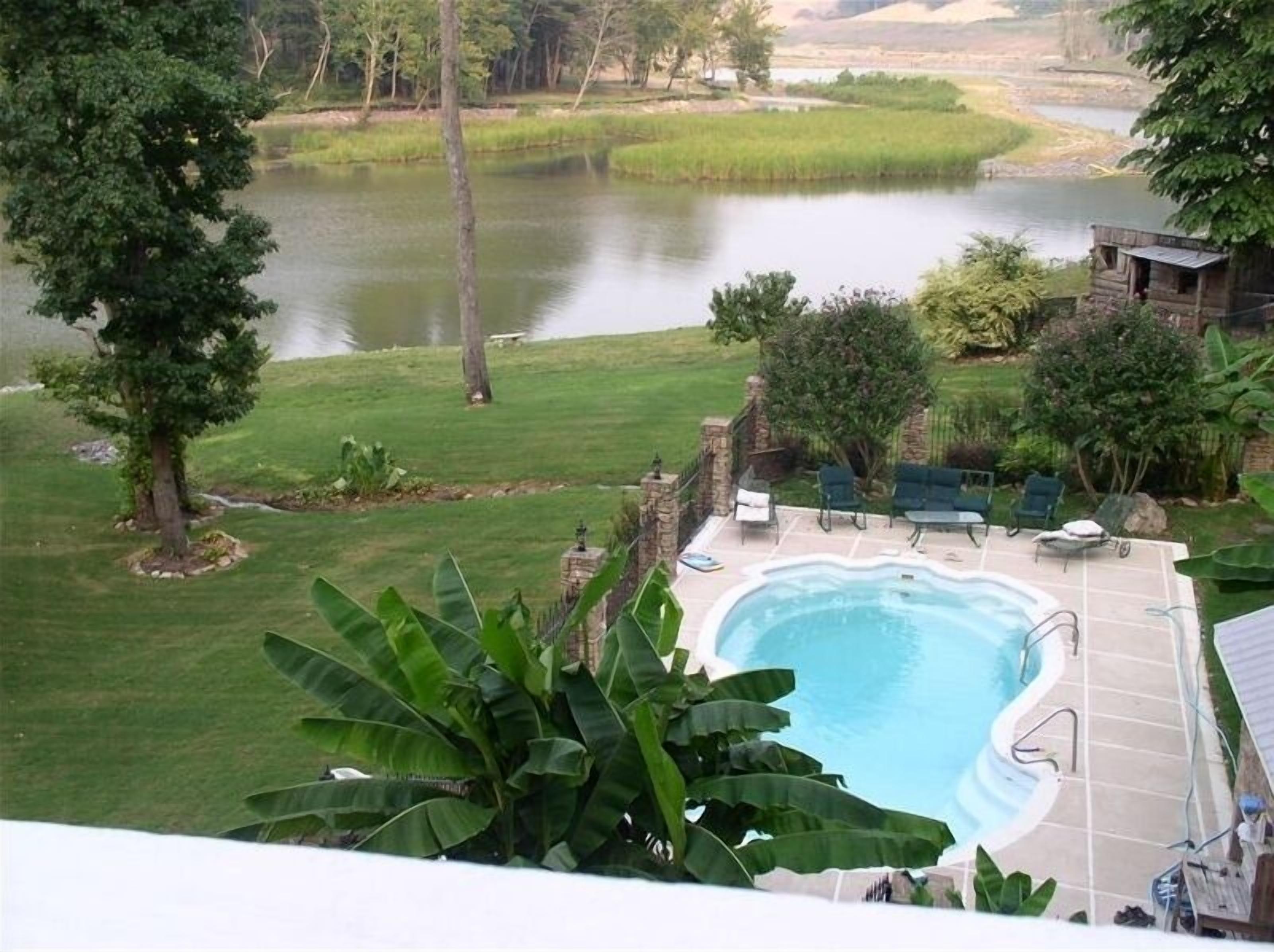 Un patio trasero con piscina, un porche con sillas y vista a un lago.