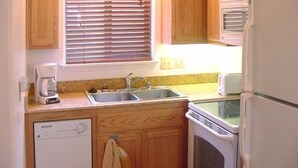 A compact kitchen with wooden cabinets, a built-in dishwasher, a double sink, and a stove.