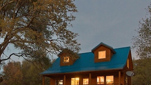A wooden cabin with a blue roof, a porch, and a satellite dish.