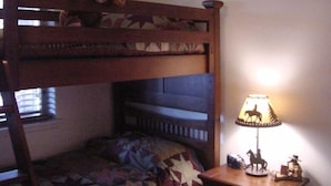 A bunk bed with a teddy bear on the top bunk, a patterned quilt on the bottom, and a lamp with a cowboy figure on the nightstand.
