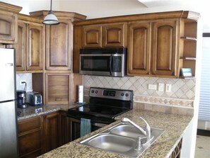 Compact kitchen with a classic design, featuring a stainless steel sink, stove, and microwave, as well as a granite countertop and pendant light.