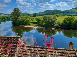 Un río con un puente de madera, abundante vegetación y un castillo al fondo.