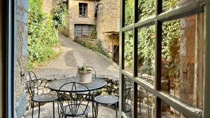 Une terrasse extérieure avec une table et des chaises, entourée de bâtiments en pierre et de verdure.