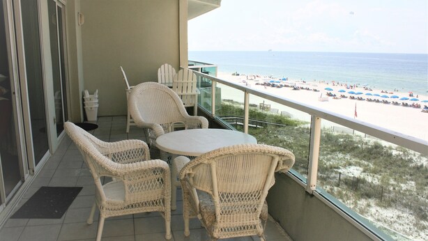 A balcony with wicker furniture, a glass door, and a view of the beach.