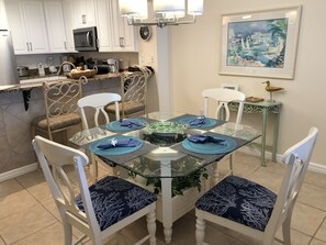 A dining area with a glass table, white chairs, and blue placemats.