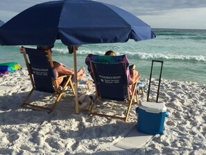 Two beach chairs with umbrellas at Pelican Beach Resort, a cooler, and a beach setting.