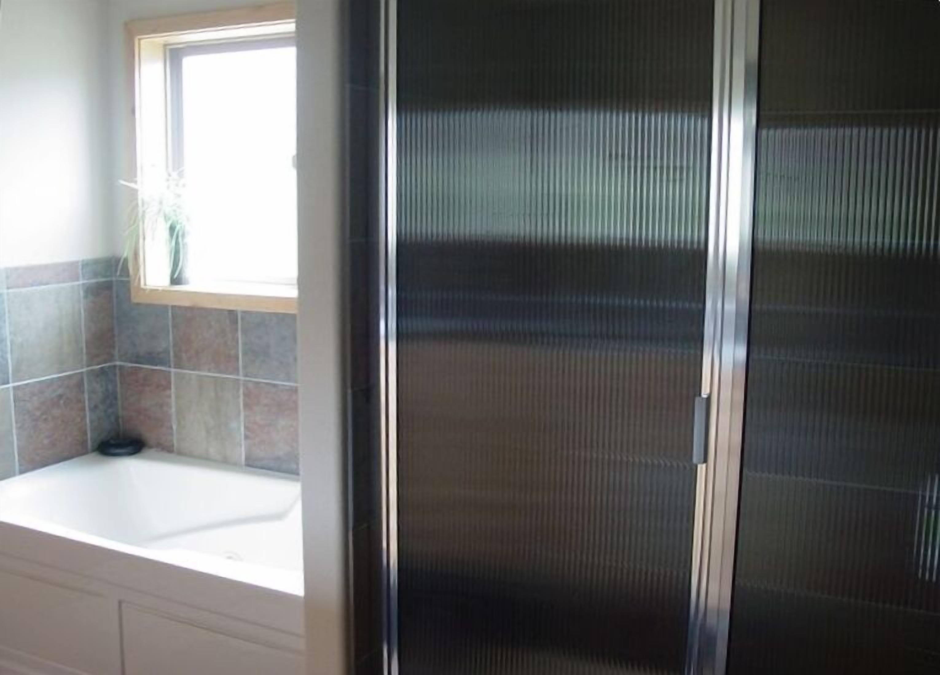 Ein Badezimmer mit einem weißen Waschbecken, einem Fenster mit Pflanze und einem Duschbereich mit einer Metalttür.
