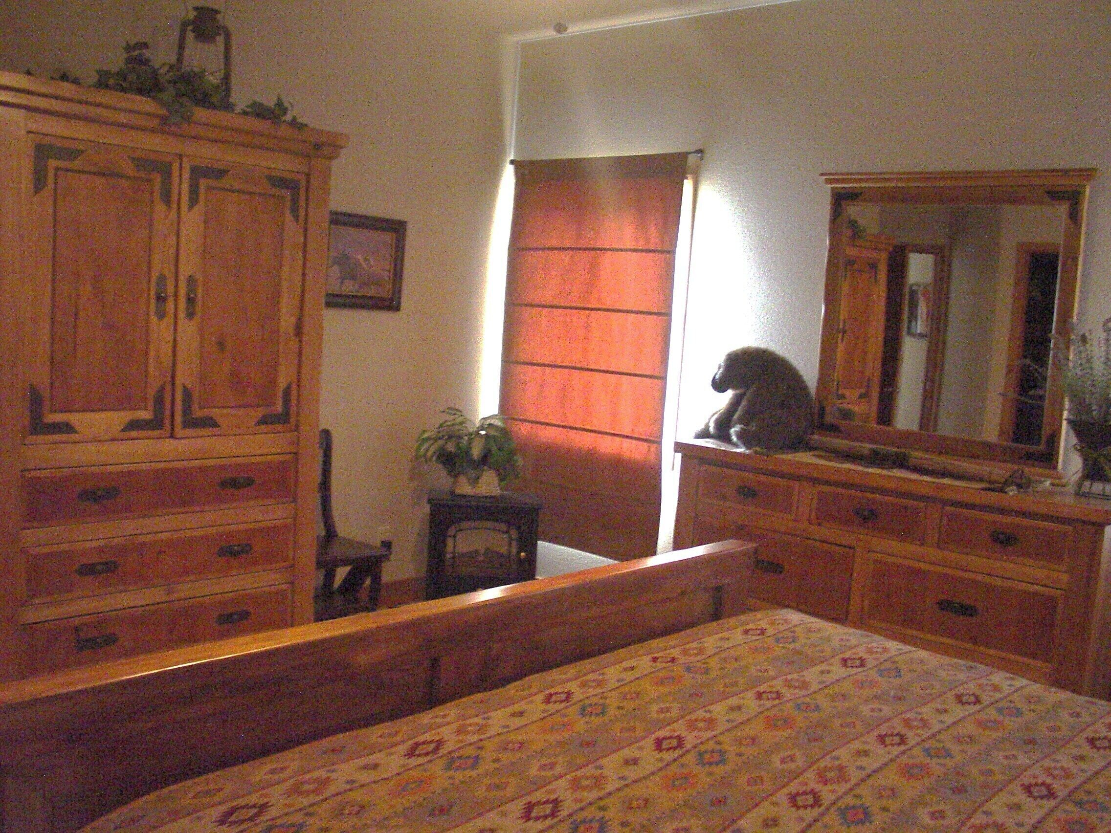 Een slaapkamer met een houten bed, een dressoir, een spiegel en een raam met gordijnen.