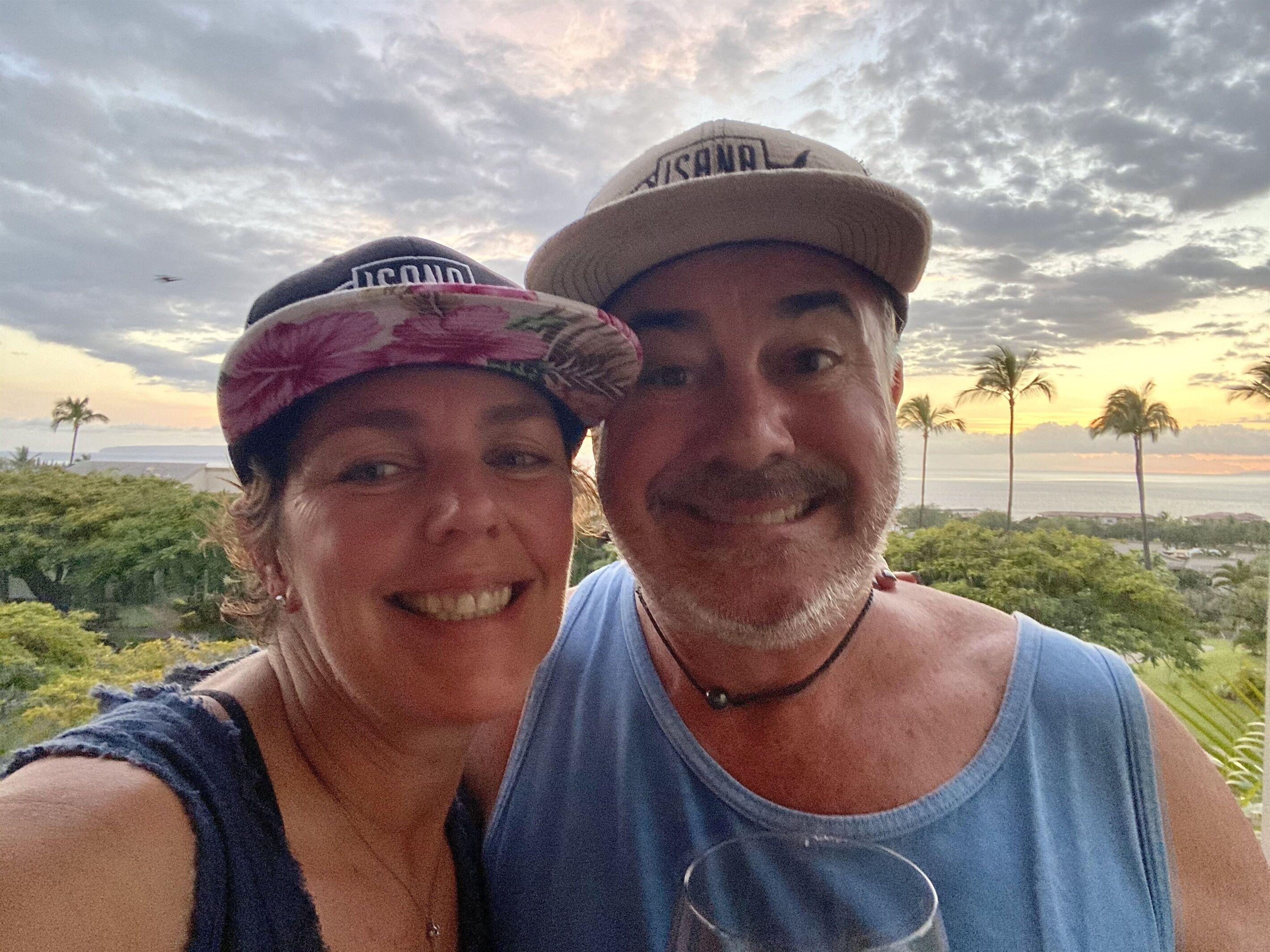A couple posing with a scenic view of palm trees and a body of water in the background.