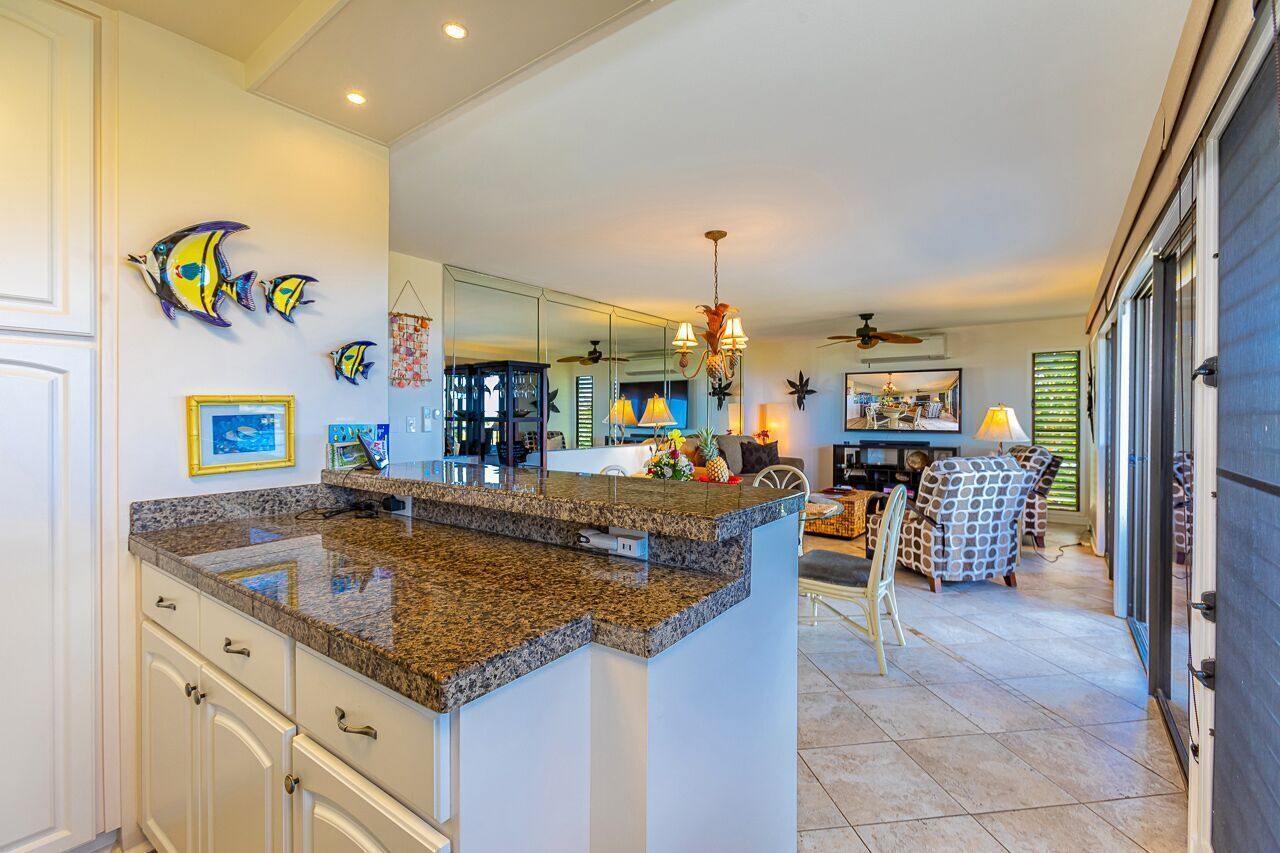 A kitchen with granite countertops, a dining area with chairs, and a large window.