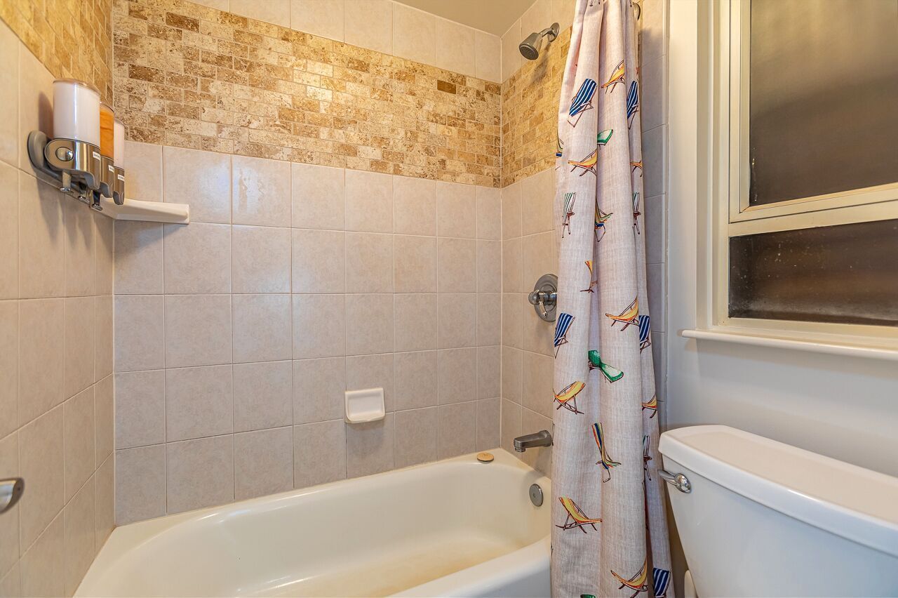 A bathroom with a bathtub, a shower, and a toilet. There is a towel rack and a soap dish on the wall.